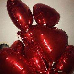 red heart shaped balloons are in the middle of a pile on top of a table