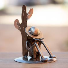 a small metal figurine sitting on top of a wooden table next to a tree