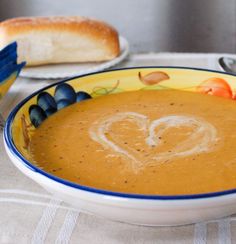 a bowl of soup with two hearts drawn on the top and bread in the background