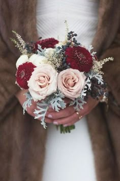 a bride holding a bouquet of red and white flowers in her hands with fur coat on the background