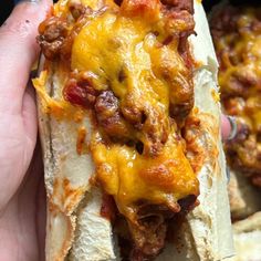 a hand holding a hot dog covered in cheese and chili