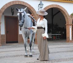 a woman standing next to a gray horse in front of a white and brown building