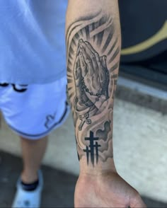 a person with a tattoo on their arm holding a cross and praying hands in front of him