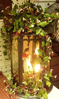 an old fashioned lantern is adorned with greenery and lit candles for the holiday season