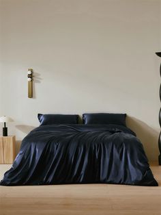 a bed with blue sheets and pillows in a room next to a tall wooden floor lamp