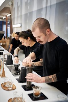 a man and woman are preparing coffee at the counter in front of some other people