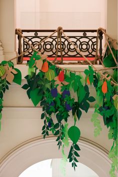 some green leaves and oranges hanging from a branch in front of a red window