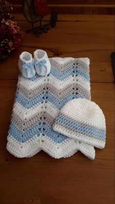 a crocheted baby blanket and booties sitting on top of a wooden floor