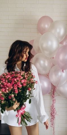 a woman standing in front of a bunch of balloons and holding a bouquet of flowers