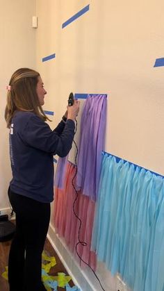 a woman is painting on the wall with blue and pink streamers in front of her