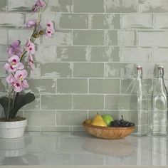 a bowl of fruit sitting on top of a kitchen counter next to bottles and flowers