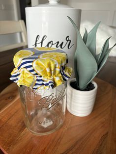 a glass jar with flowers in it sitting on a table next to a potted plant