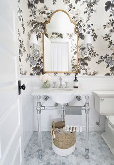 a white bathroom with floral wallpaper and mirror above the sink, along with a wicker basket on the floor