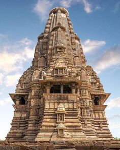 an ornate stone structure with statues on the top and side walls, in front of a blue cloudy sky