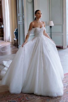 a woman in a white wedding dress standing on a carpeted floor with an ornate chandelier