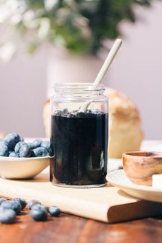 a glass jar filled with blueberries sitting on top of a wooden table next to bread