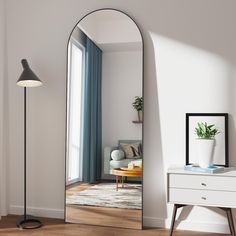 a mirror sitting on top of a wooden floor next to a white dresser and lamp