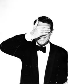 a black and white photo of a man in a tuxedo covering his eyes