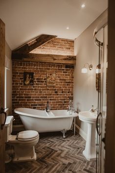 a bathroom with a brick wall and white bathtub next to a toilet in the corner