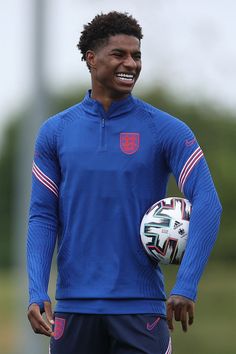 a young man holding a soccer ball in his right hand and smiling at the camera