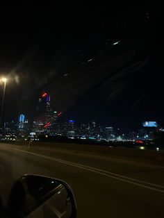 the city skyline is lit up at night from an empty highway with cars driving on it