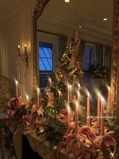 a decorated christmas tree in front of a mirror with lit candles and bows on it