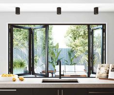 a kitchen with black cabinets and white counter tops next to an open patio door that leads out onto the backyard