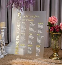 a seating chart with flowers in a vase next to candles and other decor items on a table