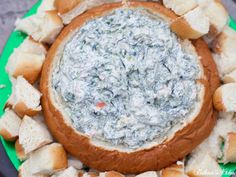 a dip in a bread bowl surrounded by croutons on a green platter