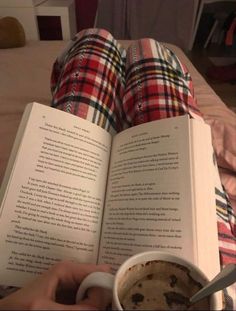 someone is reading a book and holding a cup of coffee while laying on the bed