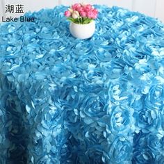 a round table covered in blue ruffled cloth with a vase of flowers on top