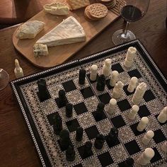 a chess board with pieces of cheese and wine glasses on the table next to it