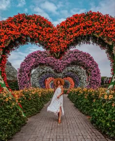 a woman in a white dress and straw hat walking down a pathway lined with flowers