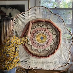 a woman is working on a large woven art piece in front of a glass window