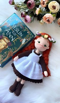 a crocheted doll next to a book on a white furnishing with flowers