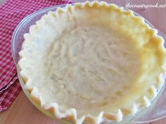 an uncooked pie crust sitting on top of a glass plate next to a red and white checkered table cloth