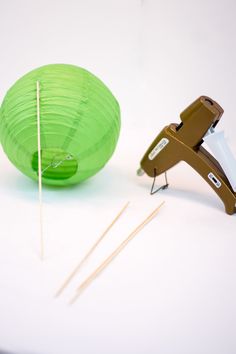 a green paper lantern and some knitting needles on a white table with a pair of scissors