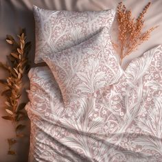 a bed covered in pink and white sheets next to a plant on top of it