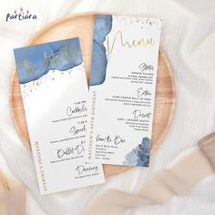 two blue and gold wedding menus on a wooden plate