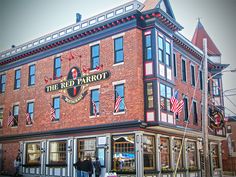 two people are standing in front of the red parrot restaurant on main street, with american flags hanging from the roof