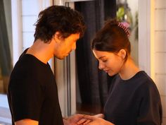 a man and woman standing next to each other in front of a window looking at their cell phones