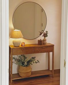 a wooden table topped with a mirror and potted plant next to a lamp on top of a hard wood floor