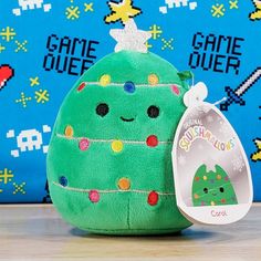 a green christmas tree stuffed animal next to a game character pillow with a tag on it