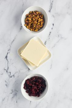 three bowls filled with nuts and cheese on top of a marble countertop next to two white plates