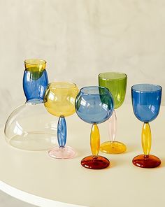 five colorful glass goblets sitting on top of a white table next to each other