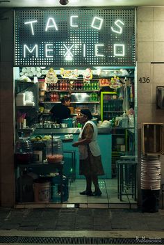 a woman standing in the doorway of a mexican food shop at night with neon lights