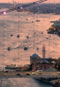 boats are floating on the water in front of a city with lights hanging from it's sides