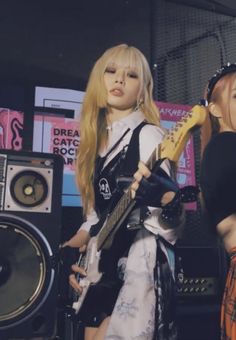 two dolls are standing next to each other in front of speakers and microphones, one is holding an electric guitar