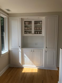 an empty kitchen with white cabinets and wood floors