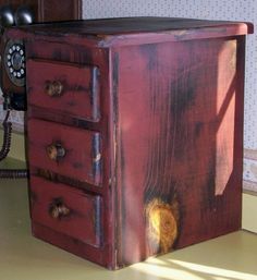 an old red wooden cabinet with two drawers and a phone on the wall behind it